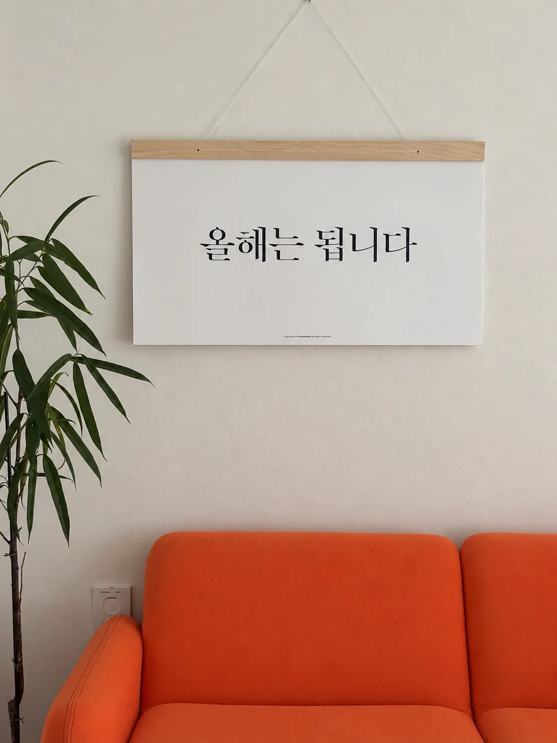 주황 소파 위 벽에 걸린 우드 스틱 캘린더
