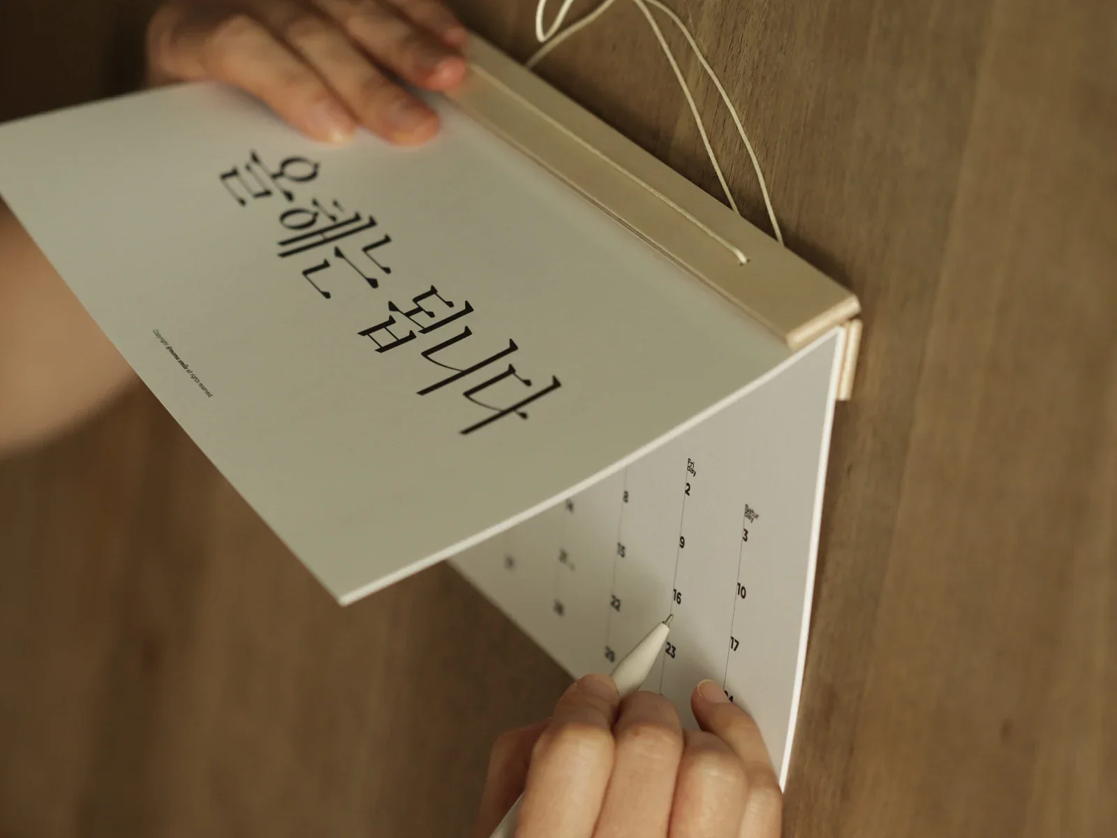 원목 테이블에 둔 우드 스틱 캘린더의 장을 넘기는 모습